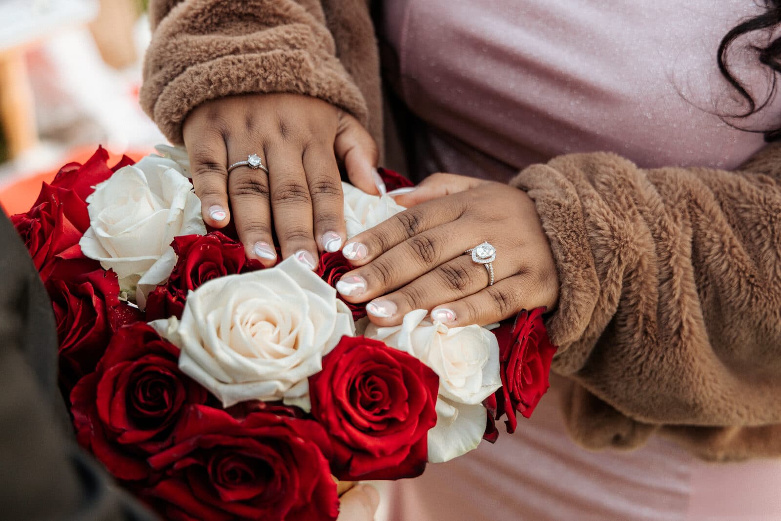 Couple's hands with engagement rings resting on a bouquet of red and white roses