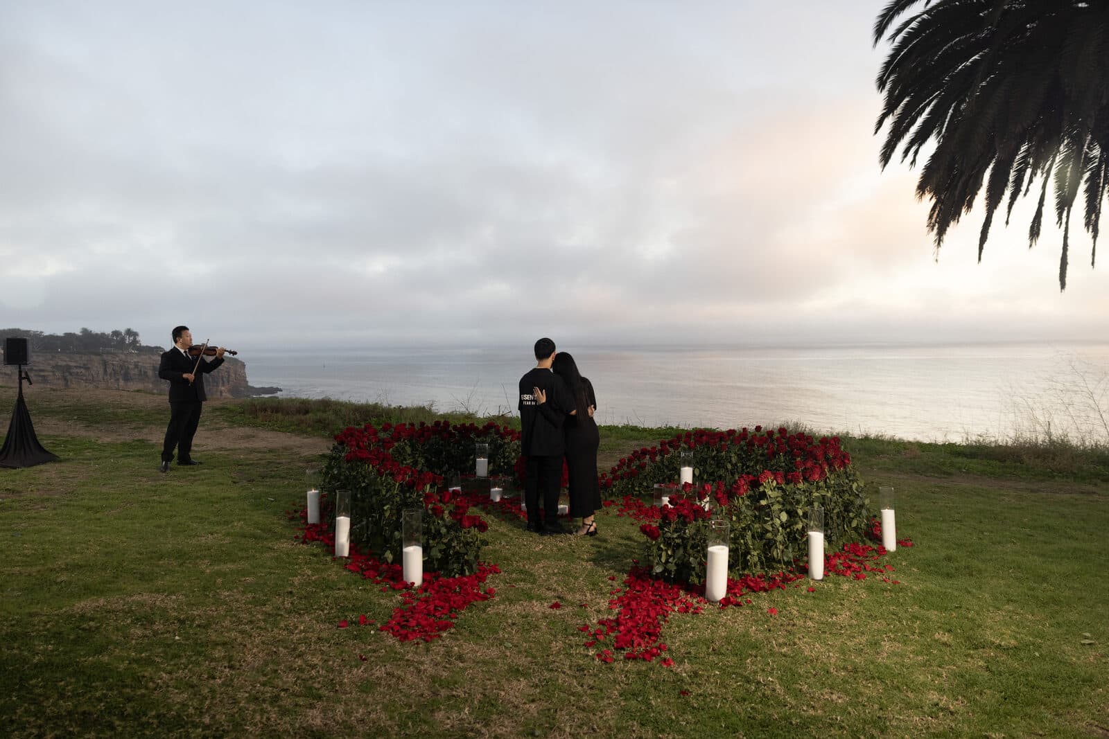 Oceanfront proposal at golden hour with a live violinist and rose-petal heart