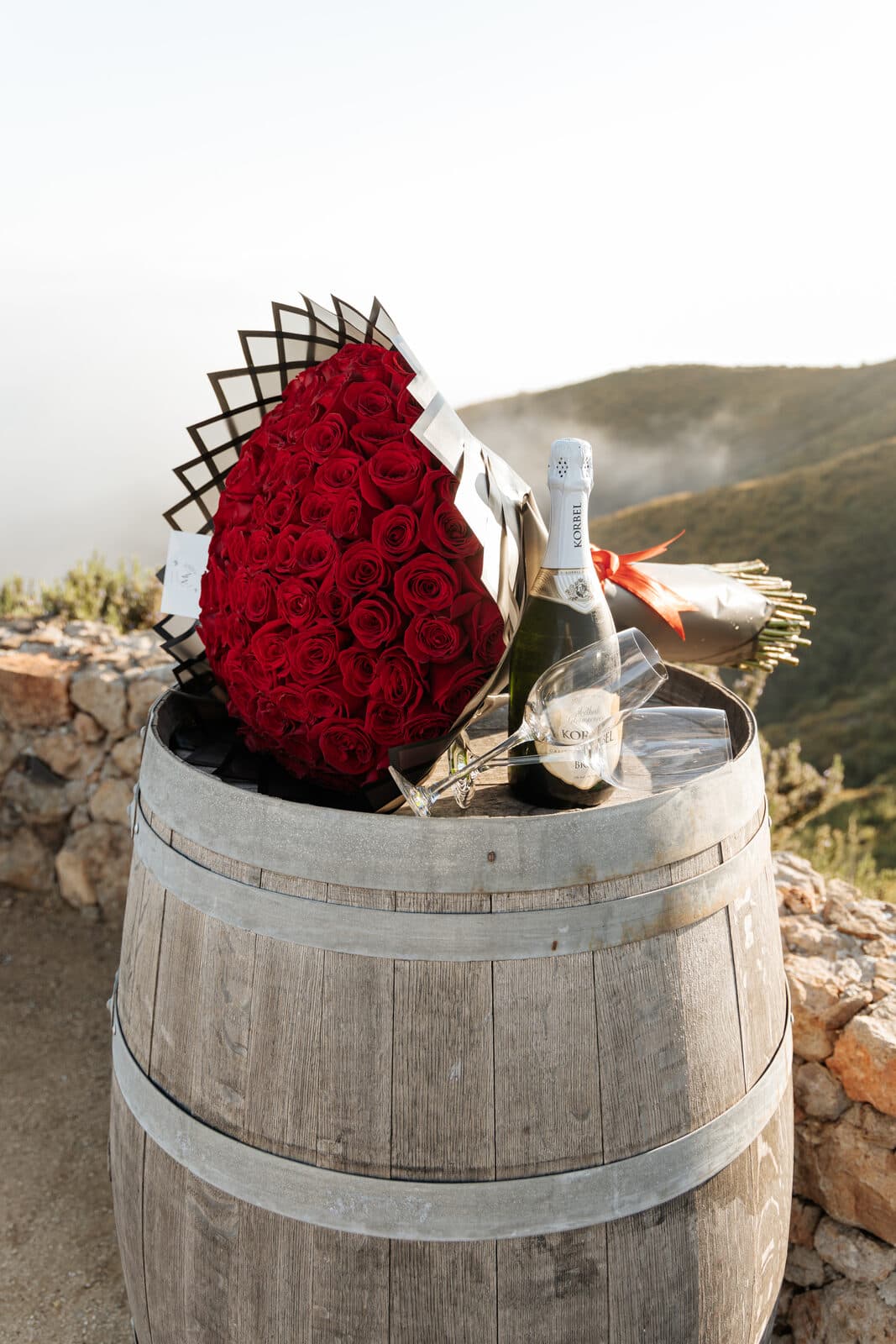 Red roses and champagne on a wine barrel at a hilltop proposal in Malibu