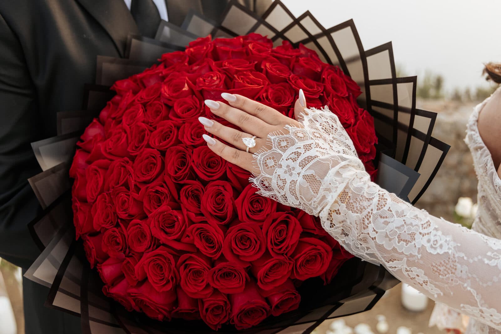 Bride's hand with engagement ring resting on a large bouquet of red roses