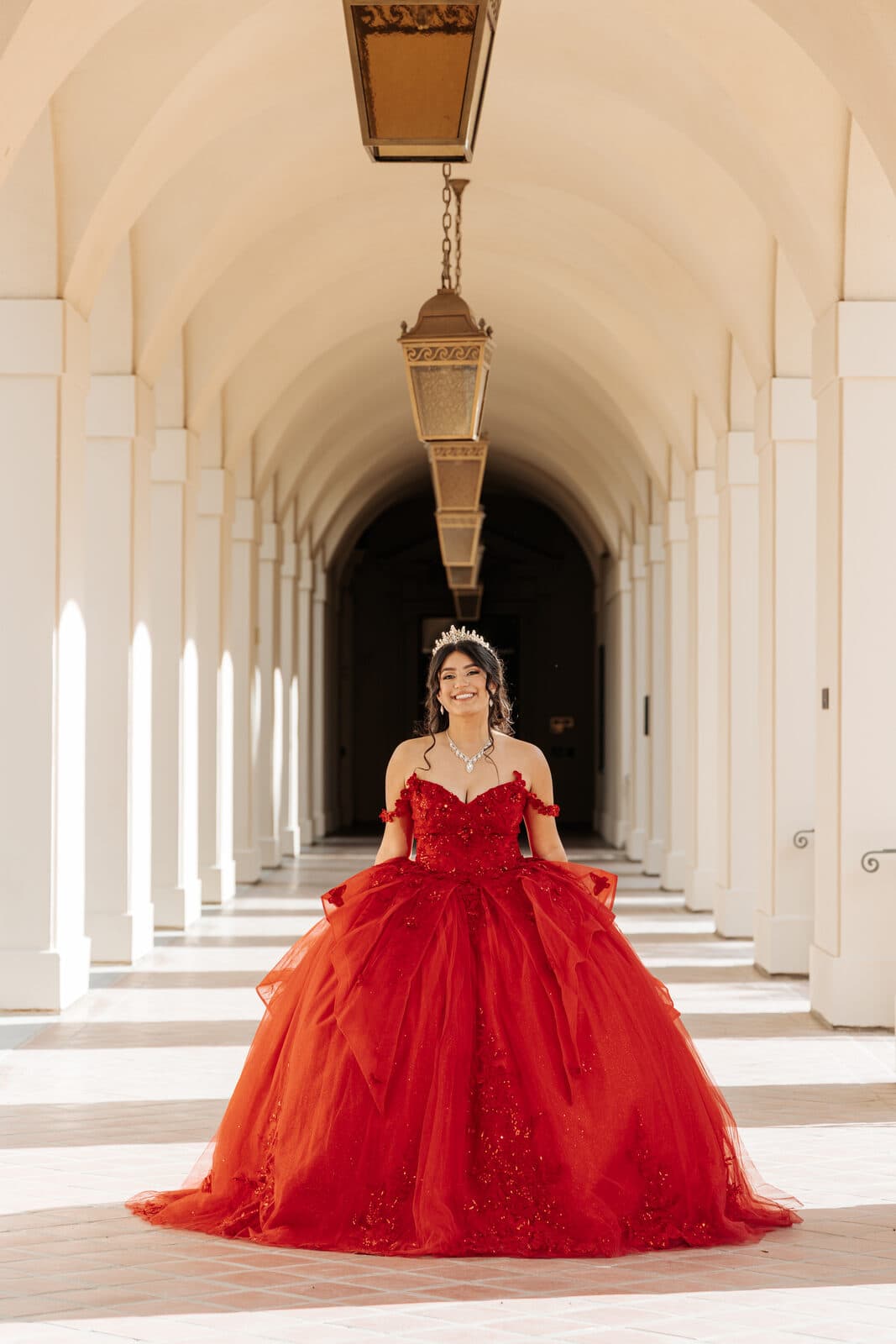 Quinceañera in a flowing red gown beneath a historic Pasadena City Hall archway