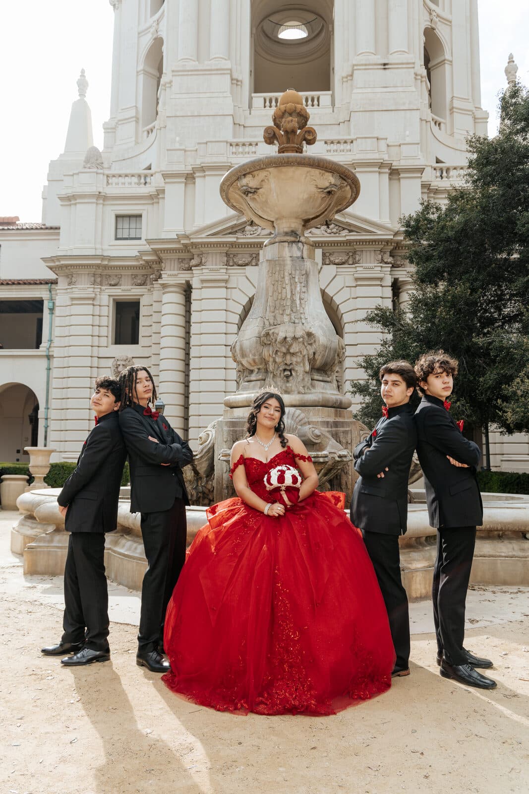 Quinceañera in a red ball gown with her court in front of a Pasadena fountain